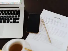 Laptop, telefon i dokument "Contract" leżą na biurku. Czy to ta umowa na stałe?