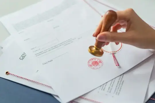 Dłoń z pieczęcią notarialną na dokumentach. To może być ważny krok, jak intercyza po ślubie, zabezpieczający przyszłość.