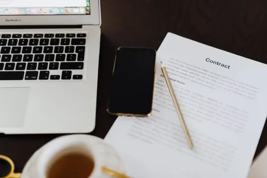 Laptop, telefon i dokument "Contract" leżą na biurku. Czy to ta umowa na stałe?